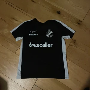 Svart AIK fotbollströja från Nike - Säljer en svart AIK fotbollströja från Nike med vita detaljer. Tröjan har korta ärmar och är tillverkad i Dri-FIT material för optimal komfort. Perfekt för alla AIK-fans som vill visa sitt stöd. Logotyper från Nike, Stadium och Truecaller pryder framsidan. Köpte den för ungefär 700kr tror jag och säljer för 350kr