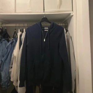 Mörkblå cashmere hoodie från John Henric - Säljer en lyxig mörkblå hoodie från John Henric i 100% cashmere. Den har en dragkedja framtill och huva. Passar både till avslappnade och mer uppklädda tillfällen. Knappt använd, köptes för 2500 kr!