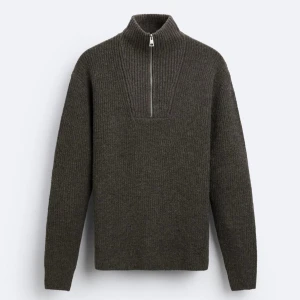 Mörkgrå stickad tröja med dragkedja - Säljer en stilren mörkgrå stickad tröja med dragkedja i halsen. Perfekt för kyliga dagar med sin höga krage och långa ärmar. Tröjan har en ribbad struktur upptill som ger en snygg detalj. Passar både till vardags och mer avslappnade tillfällen.