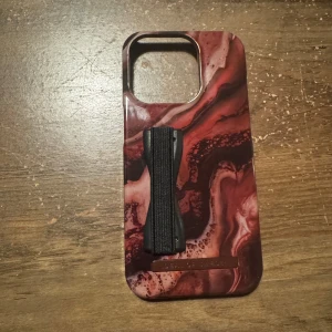 Ideal of Sweden! Marmormönstrat mobilskal med handtag - Snyggt mobilskal med marmormönster i rödbruna nyanser. Skalet har ett praktiskt elastiskt handtag för bättre grepp. Perfekt för att ge din mobil en stilren look.