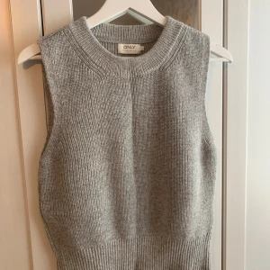 Grå stickad väst från ONLY - Säljer en stilren grå stickad väst från ONLY. Västen har en ribbad design och är perfekt för lager-på-lager-stil. Den är ärmlös och har en rund halsringning.