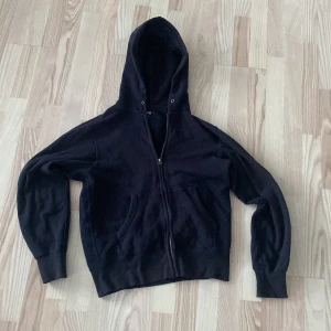Svart hoodie från Uniqlo - Säljer en svart hoodie från Uniqlo med dragkedja och huva. Den har långa ärmar och en praktisk ficka framtill. 