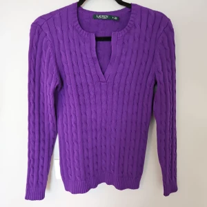 Lila stickad tröja från Ralph Lauren - Snygg lila stickad tröja från Ralph Lauren med kabelstickat mönster. Tröjan har en v-ringad hals och långa ärmar, perfekt för kyligare dagar. Ett stilrent plagg som passar till många tillfällen.