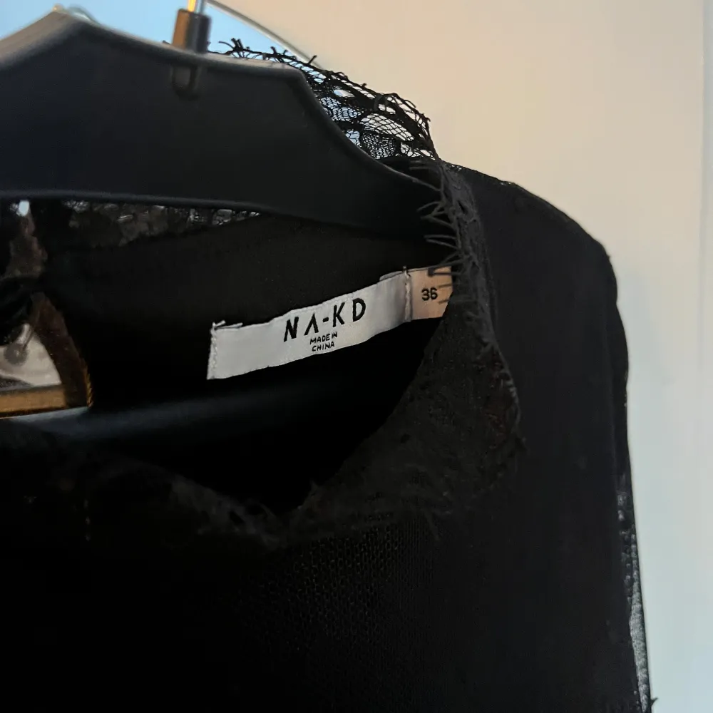 Elegant svart spetsblus från NA-KD med långa ärmar och vackra spetsdetaljer. Blusen har ett prickigt mönster på ärmarna och en fin volangkant nedtill. Perfekt för en stilfull look.. Puserot.