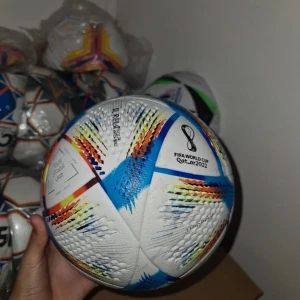 Fotboll Al Rihla FIFA World Cup 2022 - Officiell matchboll från FIFA World Cup 2022, Al Rihla från Adidas. Bollen har en vit bas med färgglada detaljer i blått, rött, gult och orange. Designen är modern och dynamisk, perfekt för både spel och samling.
