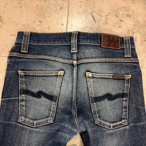 Nudie grim tim - Snygga mörkblå jeans med broderad detalj på bakfickorna. De har en klassisk femficksdesign och en bekväm passform. Perfekta för en avslappnad stil. Hör av dig vid minsta lilla fundering!storlek 31/32