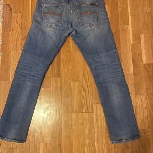 Blå jeans från nudie jeans - Säljer ett par klassiska blå jeans från nudie jeans. De har en straight passform och är tillverkade i denim med snygga detaljer som broderade bakfickor. Perfekta för en avslappnad stil. Skick enligt bilder