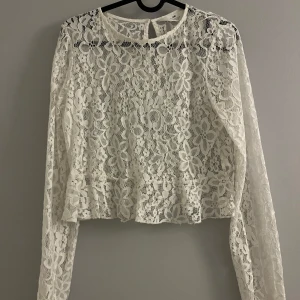 Vit spetsblus - Säljer en vacker vit spetsblus med blommigt mönster. Blusen har långa ärmar och en lätt croppad passform. Perfekt för en elegant look.