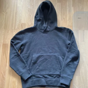 Svart hoodie från Sail Racing - Säljer en svart hoodie från Sail Racing. Den har en klassisk design med en stor ficka framtill och en bekväm huva. Perfekt för en avslappnad stil.