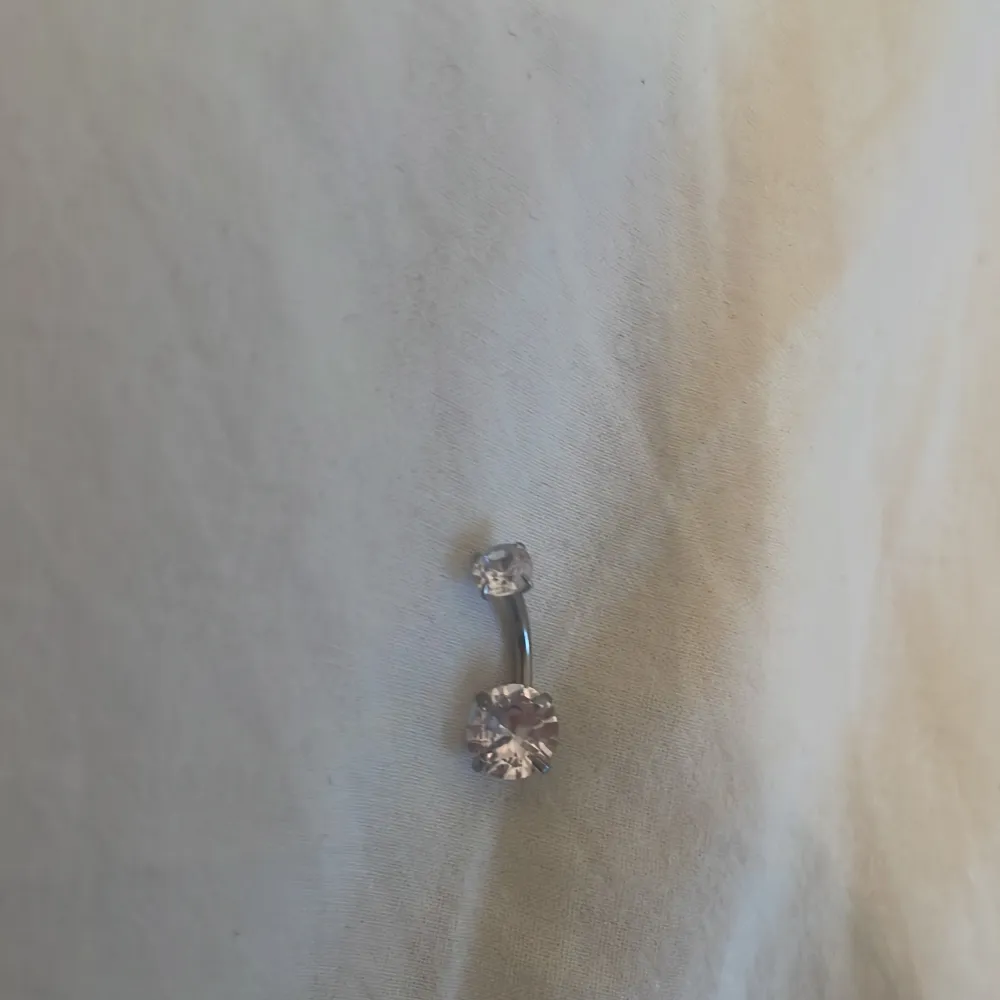 Snygg navelpiercing i silverfärg med två glittrande stenar. Perfekt för att ge en extra touch till din stil. Den böjda formen gör den bekväm att bära.. Asusteet.