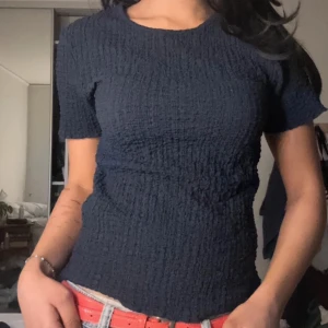 Mörkblå ribbad topp - Säljer en mörkblå ribbad topp i polyester och elastan. Toppen har korta ärmar och en tight passform, perfekt för en stilren look. Den är enkel och bekväm att bära. Ny med prislapp kvar💙