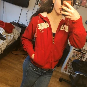 Röd hoodie från Abercrombie & Fitch - Säljer en snygg röd hoodie från Abercrombie & Fitch med dragkedja och vit text på bröstet. Den har en mysig fodrad huva och ribbade muddar vid ärmslut och nederkant. Perfekt för kyliga dagar! 🔥