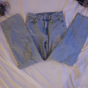 Blå jeans med slitningar - Säljer ett par blå jeans i loose straight fit med hög midja. Jeansen har coola slitningar på benen och är tillverkade i denim. Perfekta för en sommar dag!