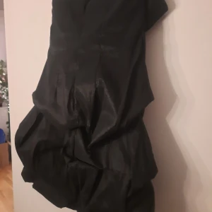 Svart axelbandslös klänning - Snygg svart axelbandslös klänning med volangdetaljer. Perfekt för en elegant kvällslook. Klänningen har en unik struktur och en chic design. Använd endast 1 gång. Nypris 1500, mitt pris 300