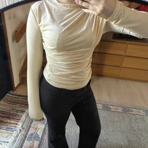 Beige långärmad topp - Säljer en stilren beige långärmad topp med rynkade detaljer i midjan. Perfekt för en elegant look. Toppen har en tight passform och är tillverkad i ett mjukt material.