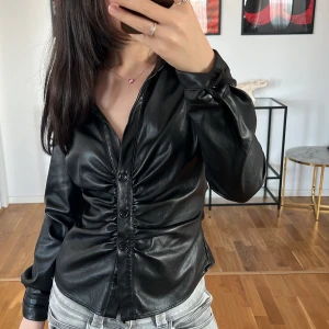 Svart skinnskjorta med knappar Zara  - Säljer en snygg svart skinnskjorta från Zara med knappar framtill. Skjortan har en tight passform och långa ärmar. Perfekt för en snygg ich  stilren look. Passar både till vardags och fest💓