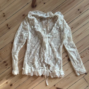 Vit spetsblus med volangdetaljer - Säljer en superfin vit spetsblus med volangdetaljer och knytning framtill. Blusen har långa ärmar och en v-ringad design. Perfekt för en romantisk look eller en festlig kväll! 💖