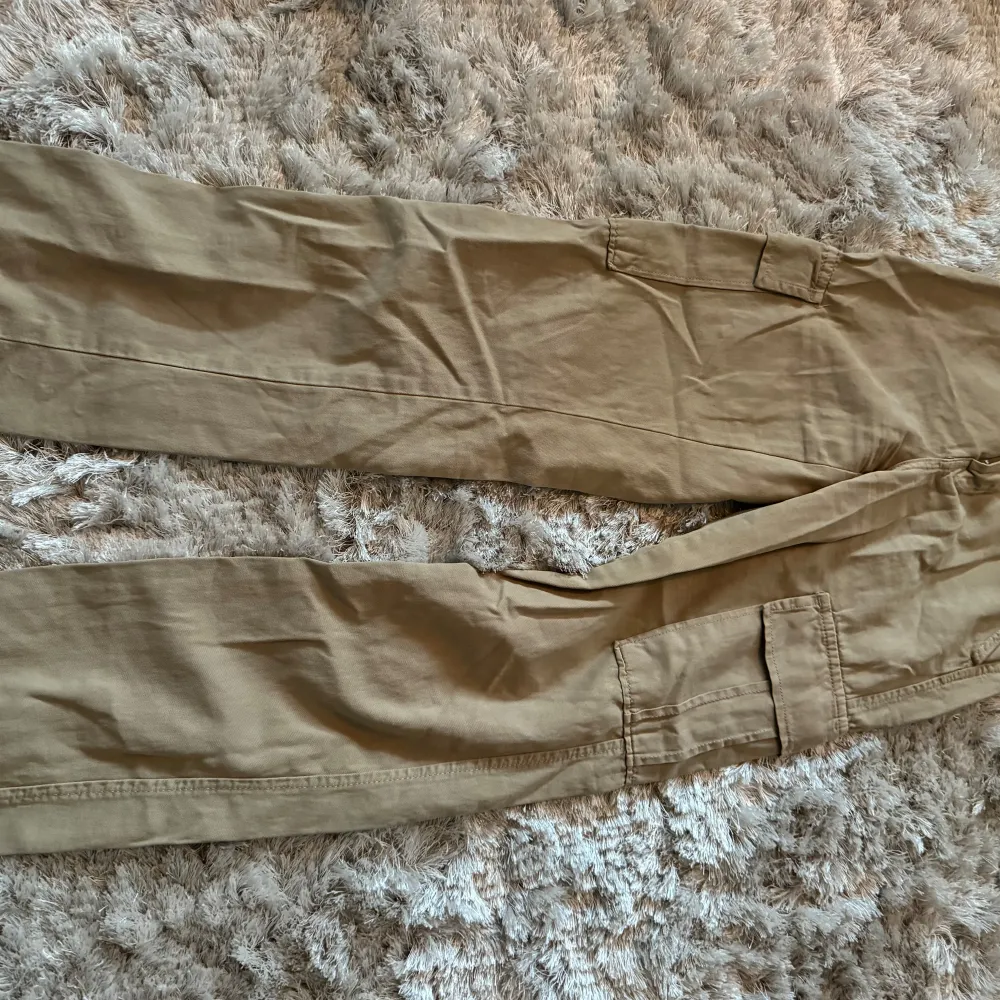 Säljer ett par snygga beige cargopants. De har flera praktiska fickor på sidorna och är perfekta för en avslappnad stil. Byxorna är i bra skick och passar perfekt för höst och vår.. Farkut & Housut.