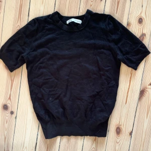 Svart tröja från Zara - Säljer en stilren svart tröja från Zara i storlek S. Tröjan är kortärmad och gjord i ett mjukt material som känns skönt mot huden. Perfekt för både vardag och festliga tillfällen! 
