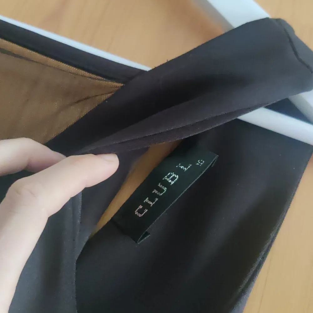 Säljer en elegant svart klänning från Club L. Den har en djup v-ringning och är ärmlös, vilket gör den perfekt för festliga tillfällen. . Mekot.
