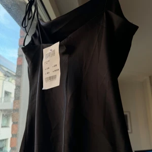 Svart axelbandslös klänning i satin från Brandy Melville - Kort svart klänning i satin med tunna band som knyts på axeln. Klänningen har ett fint fall. Köpt på Brandy Melville men aldrig använd, passar en XS eller S. 