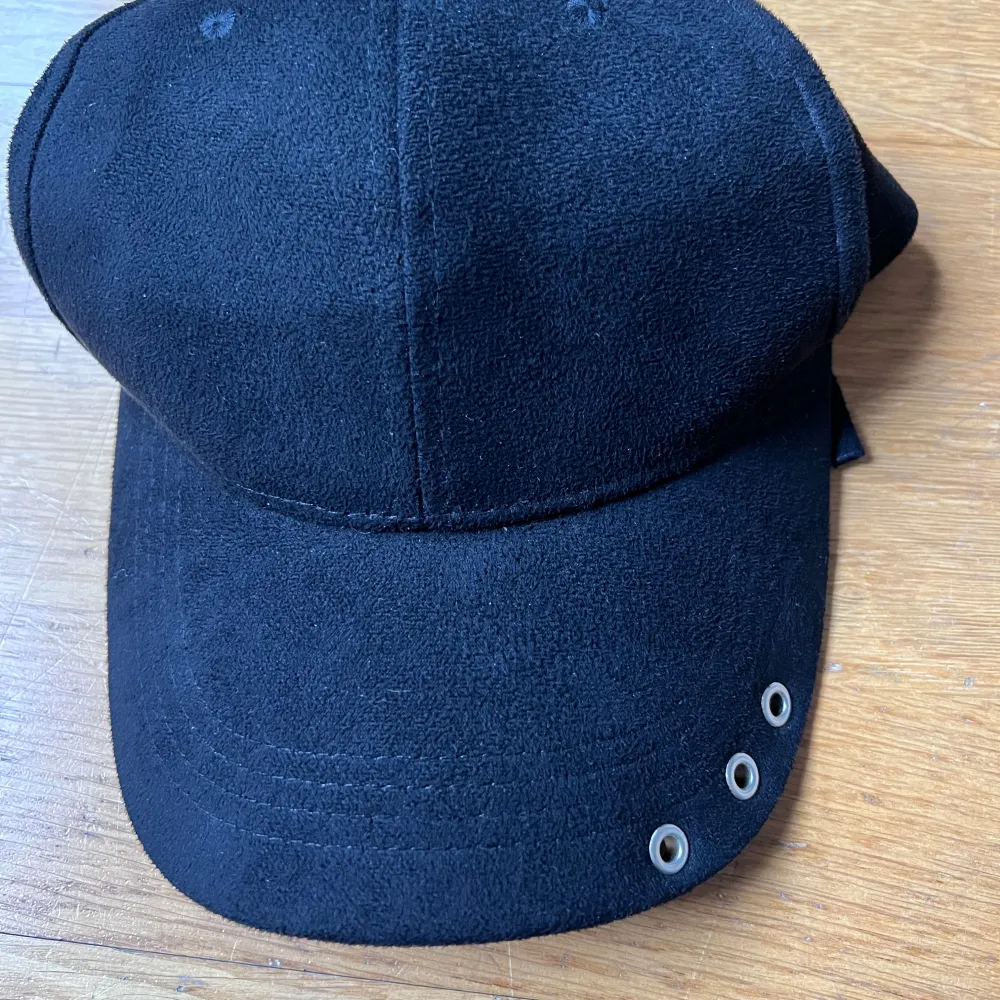 Snygg svart keps i 100% polyester med tre metallöljetter på skärmen. Perfekt för en stilren look. Tillverkad i Kina.. Asusteet.