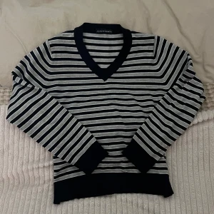 Randig tröja från Seventyone - Snygg randig tröja från Seventyone i svart och grått. Tröjan har en v-ringad hals och långa ärmar, perfekt för en stilren look. 