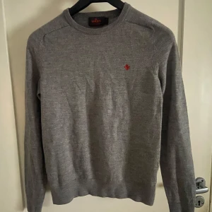 Grå merinoulltröja från Morris - Säljer en stilren grå tröja från Morris i 100% merinoull. Tröjan har en liten röd broderad logga på bröstet och rund halsringning. Storlek S men sitter som XS. Skicket är så gott som nytt! Skriv för mer info eller bilder!