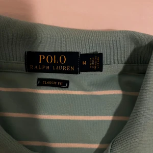 Grön- och vitrandig pikétröja från Ralph Lauren - Säljer en klassisk grön- och vitrandig pikétröja från Ralph Lauren. Tröjan har korta ärmar och en broderad logotyp på bröstet. Perfekt för en stilren och avslappnad look. Pris kan såklart diskuteras.