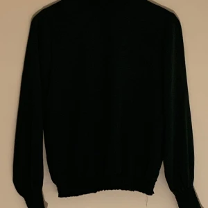 Mörkgrön blus med rynkad krage - Säljer en elegant mörkgrön blus med rynkad krage och knappar i nacken. Blusen har långa ärmar och elastiska muddar vid ärmslut och nederkant. Priset går att diskutera vid snabb affär. Kontakta gärna vid frågor eller funderingar.