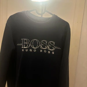  Hugo Boss - Marinblå tröja från Hugo Boss med deras ikoniska logga på bröstet. Tröjan har en slim fit passform och långa ärmar, perfekt för en stilren look.