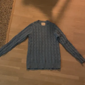 Blå stickad tröja från 157 - Säljer en snygg blå stickad tröja från 157. Tröjan har ett klassiskt flätmönster och långa ärmar. Perfekt för kyligare dagar. Passar bra till både jeans. 🧶💙