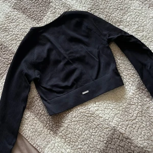 Svart ribbad tröja från Aim'n, S - Snygg och bekväm svart cropped långärmad tröja. Tröjan har en ribbstickad struktur och en rund halsringning. Perfekt för träning eller vardagsbruk. Använd en gång!