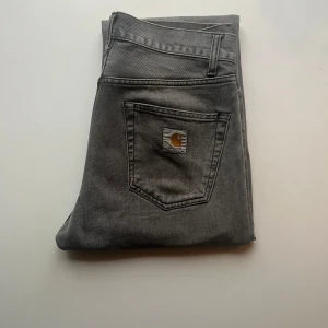 Carhartt WIP Pontaic Pant - Grå jeansbyxor från Carhartt med zipgylf. Byxorna har en rak passform och har en logotyp på bakfickan