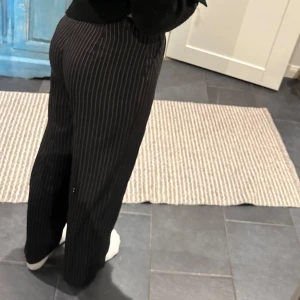 Svarta randiga byxor - Snygga svarta byxor med vita ränder. De har en klassisk straight passform och är perfekta för en stilren look. Byxorna är högmidjade och har en elegant design som passar till många olika tillfällen. Knappt använda så i jätte fint skick!!🥰