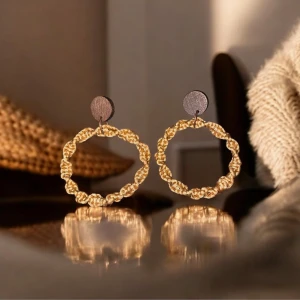 Guldiga örhängen med flätad design - Snygga guldiga örhängen knutna med makramé med en unik design. De har en rund form och fästs med en enkel platta mot örat. Perfekta för att ge en elegant touch till din outfit.