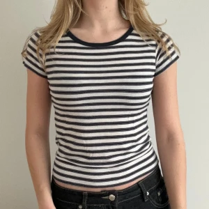 Brandy Randig t-shirt i bomull - Säljer en supermjuk stilren randig t-shirt i bomull med marinblå och vit design. Den har en rund hals och korta ärmar, perfekt för en avslappnad look. Passar bra till jeans eller shorts.