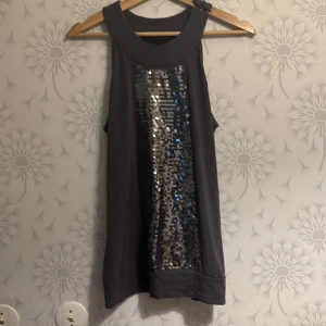 Grå ärmlös topp med paljetter från b.young - Snygg grå ärmlös topp från b.young med en glittrig paljettpanel framtill. Perfekt för att lägga till lite bling i garderoben. Tillverkad i mjukt material för en bekväm passform.