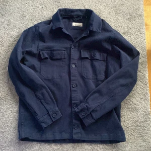 Mörkblå overshirt från Blend - Snygg mörkblå overshirt från Blend med knappar framtill och två bröstfickor. Perfekt för lager-på-lager-stil. Skjortan har långa ärmar och en klassisk krage. Köptes för 649 säljs nu för 349. Den är använd men inga tecken på det. Skriv för fler frågor eller bilder.