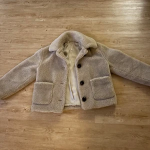 Beige teddyjacka - Mysig beige teddyjacka med stora knappar och två framfickor. Perfekt för kyliga dagar med sin fluffiga och varma design. Jackan har en klassisk krage och långa ärmar. Bra skick men för kort i armarna på mig.