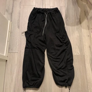 Svarta mjukisbyxor med snörning - Svarta mjukisbyxor med elastisk midja och snörning. Byxorna har 4 fickor och justerbara benslut för en bekväm passform. Perfekta för en avslappnad stil.