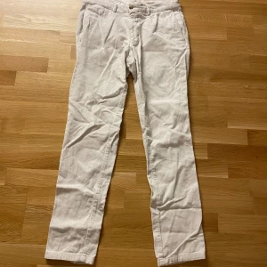 Beige/Vita manchesterbyxor från Tiger of Sweden - Snygga vita/beige byxor från Tiger of Sweden med manchester mönster. Byxorna har en klassisk design med knappar och dragkedja framtill. Perfekta för en stilren look.