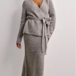 Selected Femme stickad tvådelad outfit - gråmelerad - Nytt oanvänt tvådelad outfit. En stickad kjol och en kofta från Selected Femme. Koftan har ett dekprativt band med en rosett som knyts i midjan. Elegant kjol i midilång modell. Passar både vardag och fest. Nypris ca 2400:-/set 