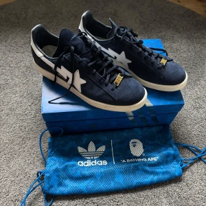 Svarta sneakers från Adidas x A Bathing Ape - Mörkblåa sneakers från samarbetet mellan Adidas och A Bathing Ape. Skorna har vita stripes och en stjärndetalj på sidan. Allt original tillkommer. Använda endast ett fåtal gånger.