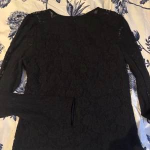 Svart spetsblus - Elegant svart spetsblus med långa ärmar och dragkedja i ryggen. Perfekt för en stilren look.