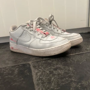 Nike Air Force i grått och rosa - Snygga Nike Air Force sneakers i grått med rosa detaljer. Skorna har klassisk snörning och en robust sula. Perfekta för en stilren look med en touch av färg.