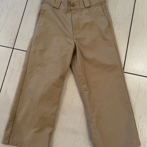 Beige byxor från Sweet Sktbs - Snygga beige byxor från Sweet Sktbs med en klassisk design. Byxorna har en rak passform och är tillverkade i ett slitstarkt material. De har knappar och bälteshällor för en justerbar passform. Perfekta för en stilren look.