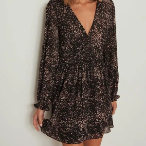 Svart och brun klänning med v-ringning - Superfin klänning med v-ringning och långa ärmar. Klänningen har ett smickrande mönster och en elastisk midja som ger en fin passform. I mycket bra skick 🥰