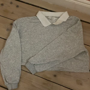 Grå tröja med krage från H&M - Säljer en grå tröja från H&M med vit krage. Tröjan har långa ärmar och en klassisk stil. Perfekt för en avslappnad look. 