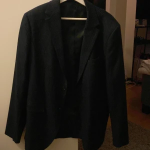 Mörkblå randig kavaj - Snygg mörkblå kavaj med diskreta ränder. Perfekt för en stilren look. Kavajen har klassiska slag och knappar framtill. Passar utmärkt till både formella och semi-formella tillfällen.